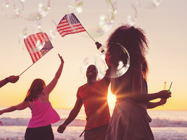 Friends celebrating on the beach at sunset with American flags and sparklers during a 4th of July event
