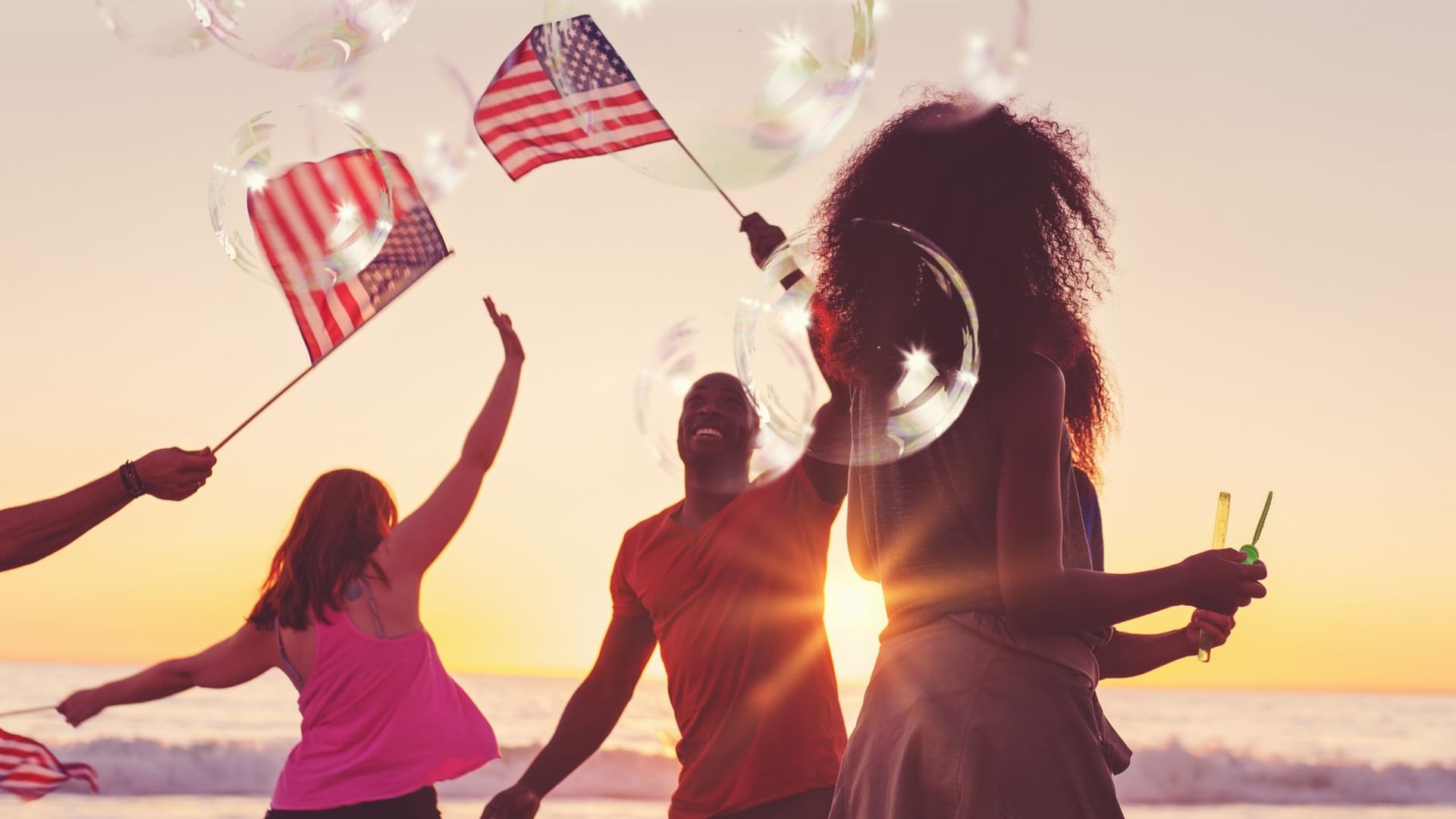 Friends celebrating on the beach at sunset with American flags and sparklers during a 4th of July event