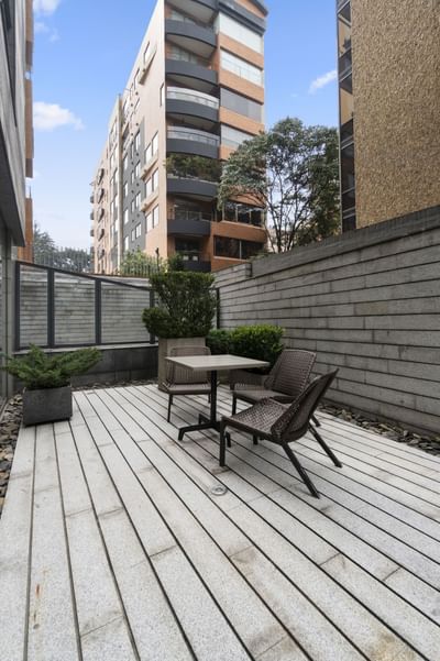 Terraza al aire libre con mesa, sillas y plantas, junto a edificio alto.