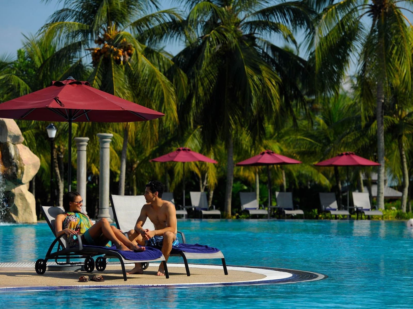 A couple on two pool chairs by the pool
