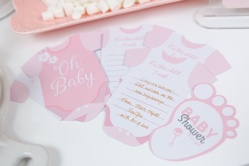 Pink baby shower invitations in the shape of onesies and a baby footprint with sweet messages at Park Hyatt Saigon