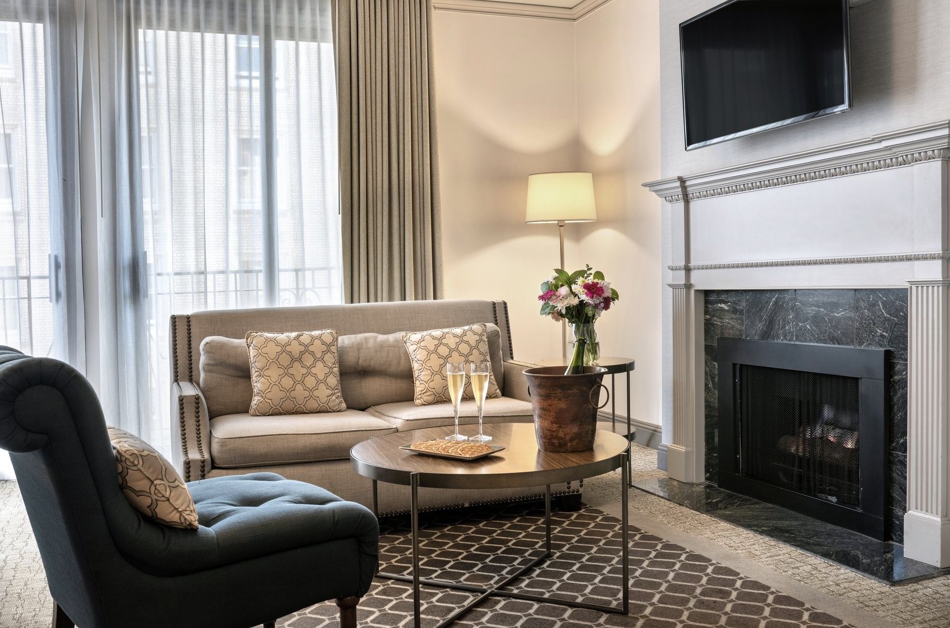 Champagne glasses on a round table near a marble fireplace at in Balcony Suite Warwick San Francisco
