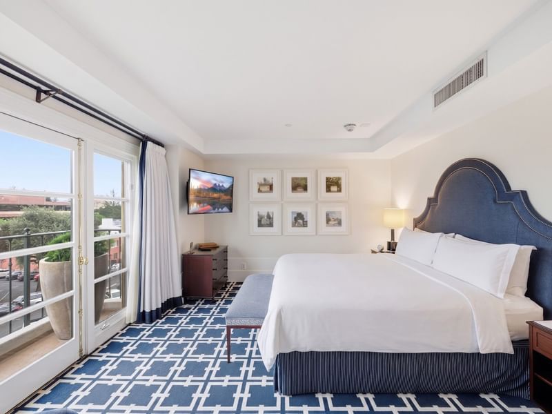 Penthouse bedroom with blue upholstered headboard, white bedding, geometric carpet, and balcony access at el PRADO Hotel.