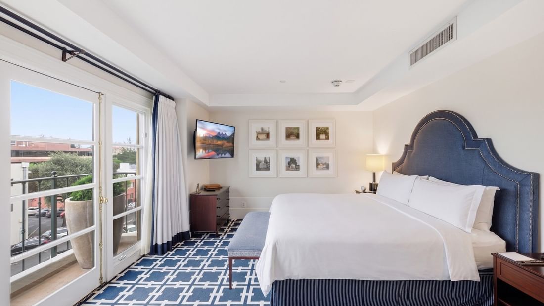 Penthouse bedroom with blue upholstered headboard, white bedding, geometric carpet, and balcony access at el PRADO Hotel.