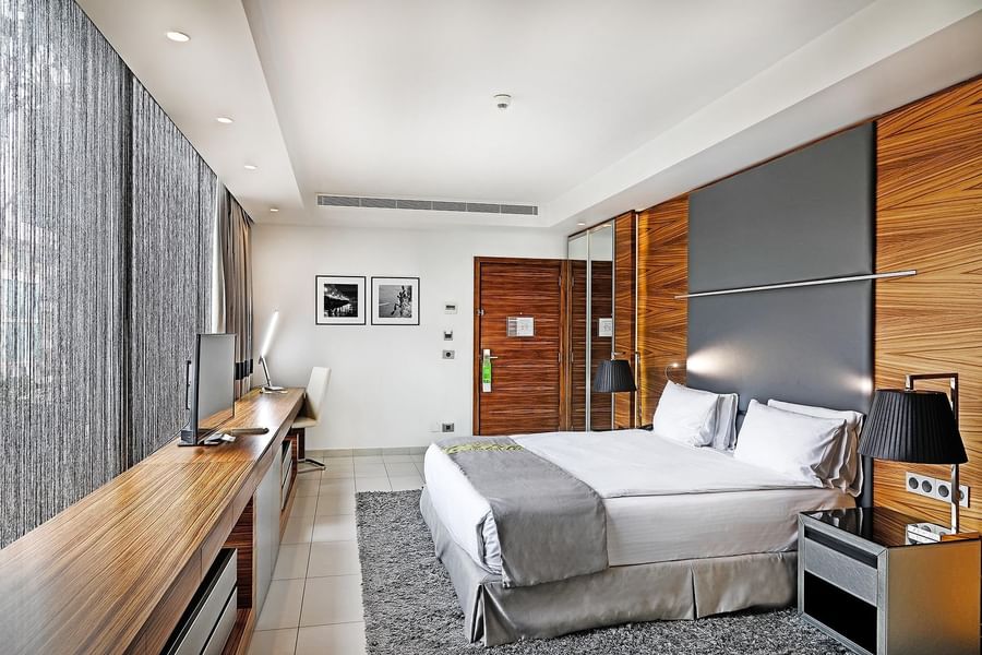 King bed by a long wooden desk under framed photos near grey curtains in Executive Room at Warwick Stone 55 - Beirut