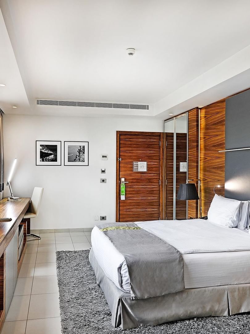King bed by a long wooden desk under framed photos near grey curtains in Executive Room at Warwick Stone 55 - Beirut