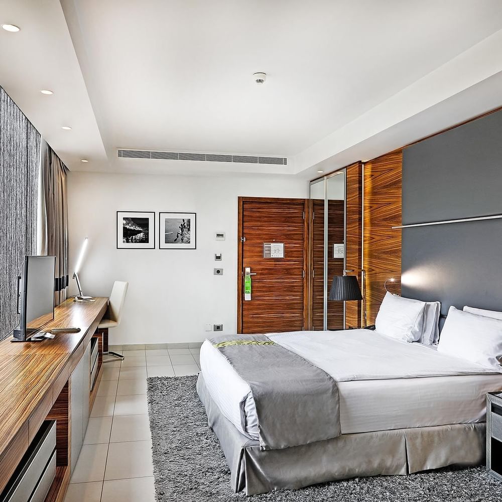 King bed by a long wooden desk under framed photos near grey curtains in Executive Room at Warwick Stone 55 - Beirut