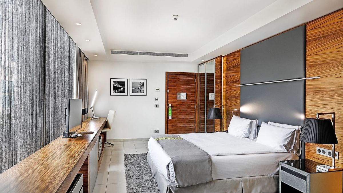 King bed by a long wooden desk under framed photos near grey curtains in Executive Room at Warwick Stone 55 - Beirut
