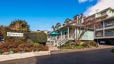 The welcoming exterior entrance and sign surrounded by vibrant flowers and greenery at Carmel Bay View Inn
