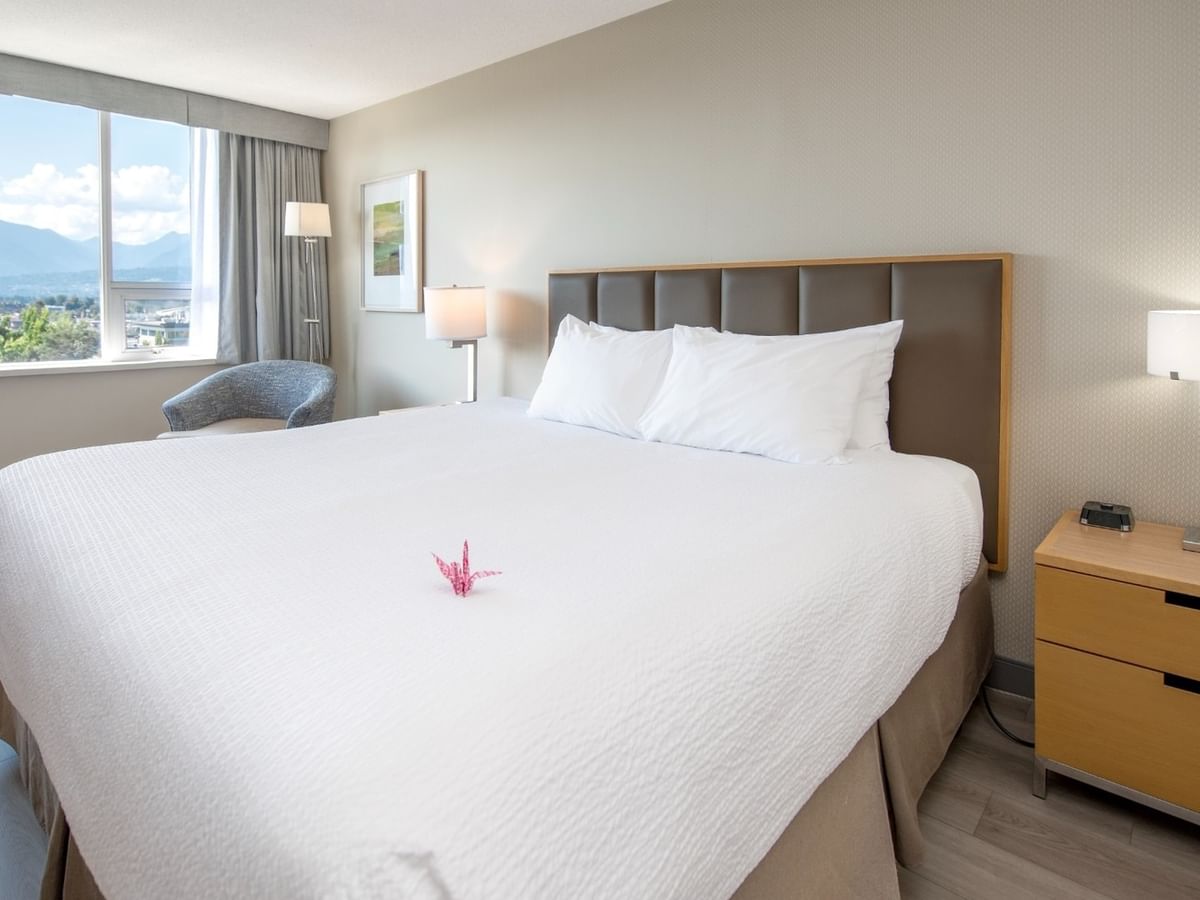 Accessible hotel bedroom with a large king bed, nightstands, and a view of mountains through a window.