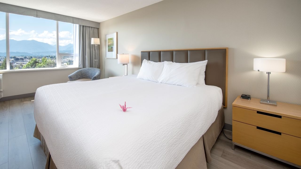 Accessible hotel bedroom with a large king bed, nightstands, and a view of mountains through a window.