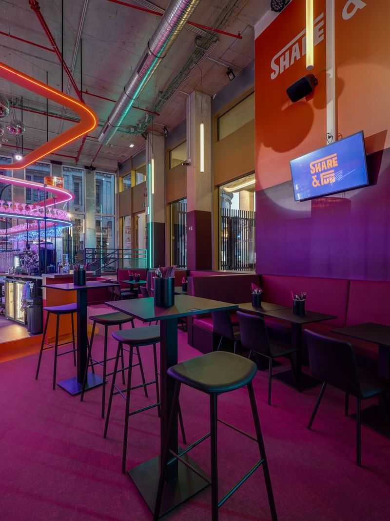 Share & Fun bar area, with stools placed by tables under neon lights and purple flooring near Warwick Grand Place Brussels