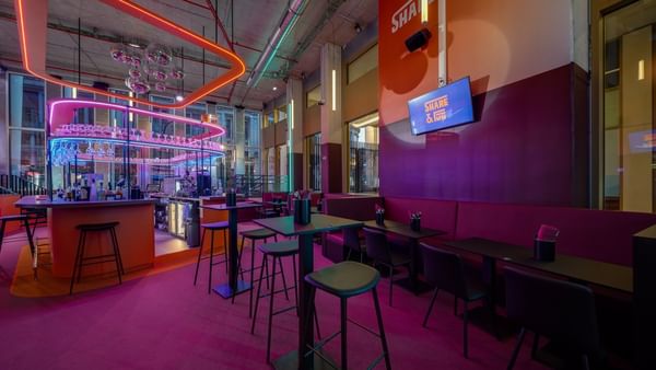 Share & Fun bar area, with stools placed by tables under neon lights and purple flooring near Warwick Grand Place Brussels