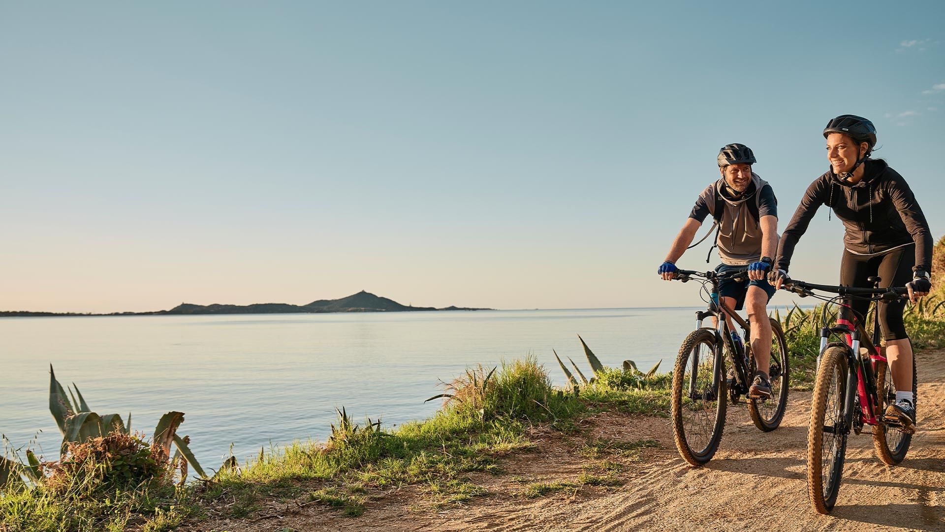 Zwei Radfahrer fahren auf einem Pfad neben dem Meer bei Sonnenuntergang.