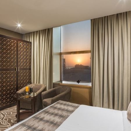 Double bed by a patterned headboard under warm spotlights in Deluxe King Sea View / Twin t Naviti by Warwick Al Khobar