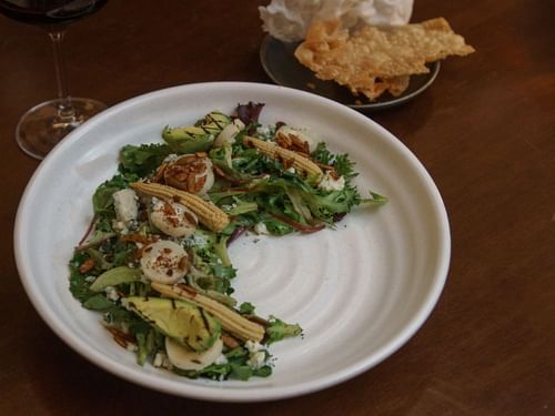Plated salad with scallops and corn, next to a glass of red wine at La Cava de Santiago in Hacienda del Mar Los Cabos.