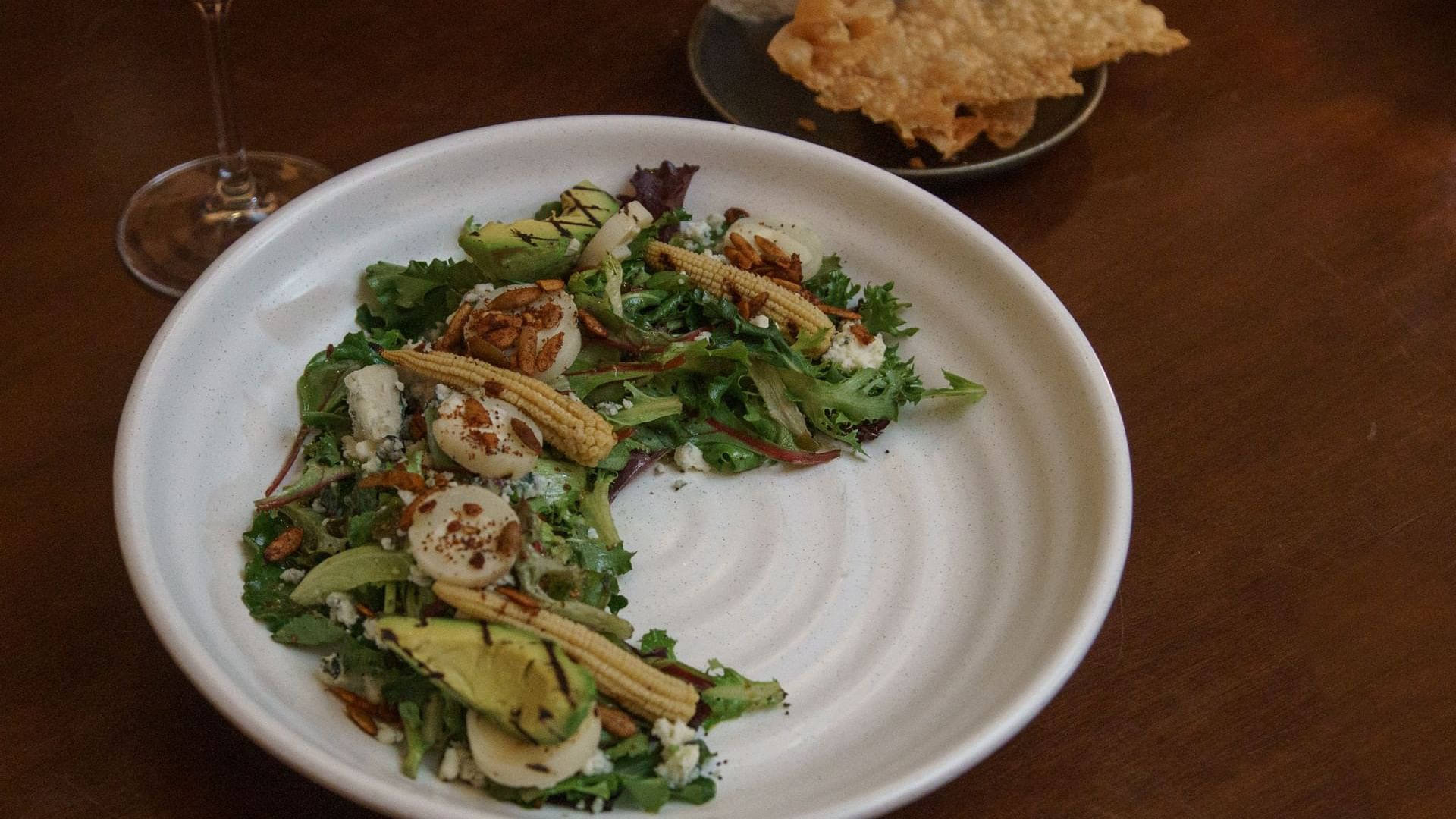 Plated salad with scallops and corn, next to a glass of red wine at La Cava de Santiago in Hacienda del Mar Los Cabos.
