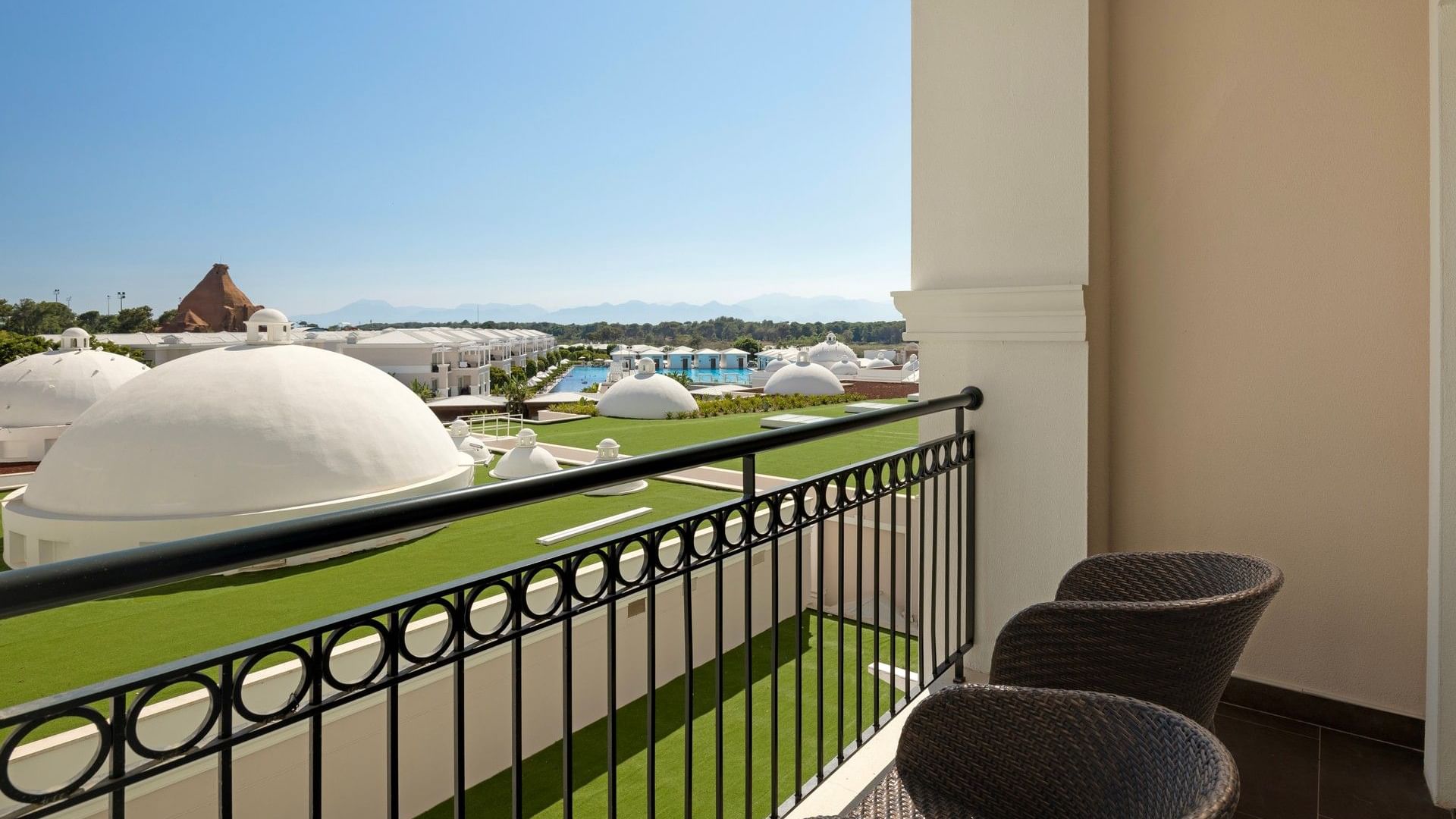 Балкон с плетеными креслами и видом на территорию отеля с белыми куполами в Titanic Deluxe Golf Belek, Анталья