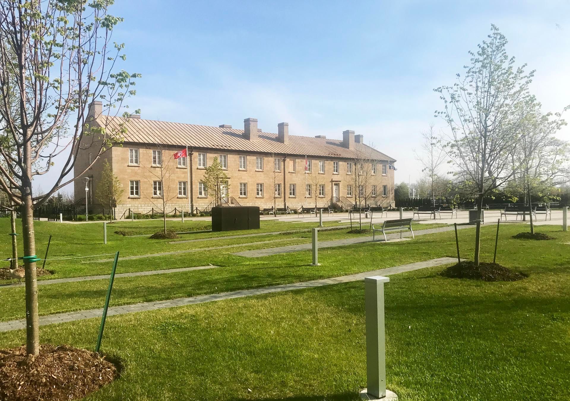 Stanley Barracks with multiple chimneys, flanked by green trees and a lawn with benches near Hotel X Toronto