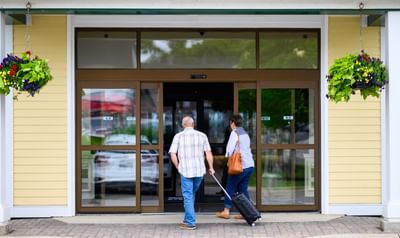 Guests walking in a doorway under hanging flower baskets, by a light yellow facade at Rodd Miramichi River