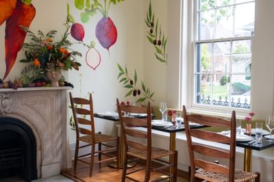 Bright dining room with vegetable mural, set tables, and fireplace mantel with floral arrangement at The Ashbrook Hotel