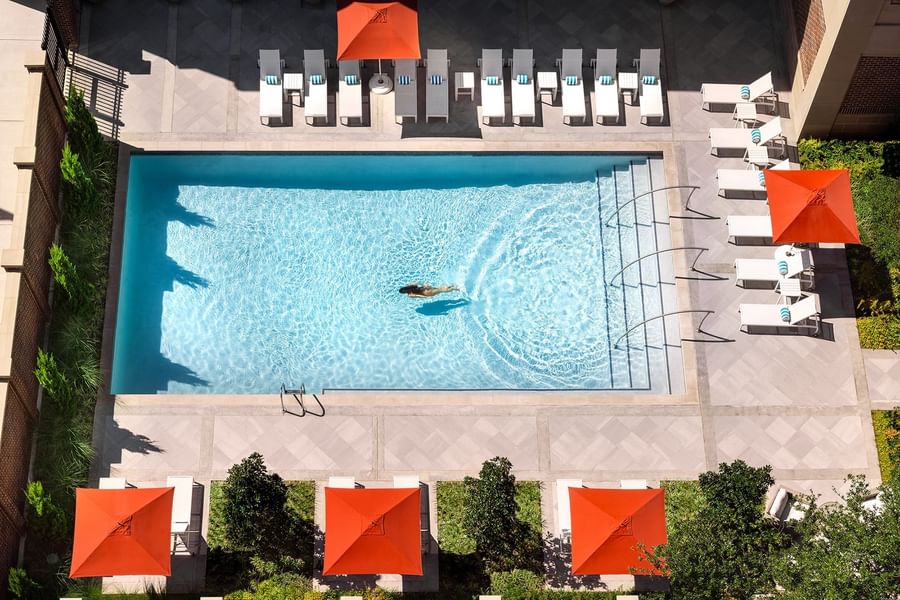 Blue pool by lounge chairs under orange umbrellas surrounding the outdoor deck at Warwick Melrose Dallas