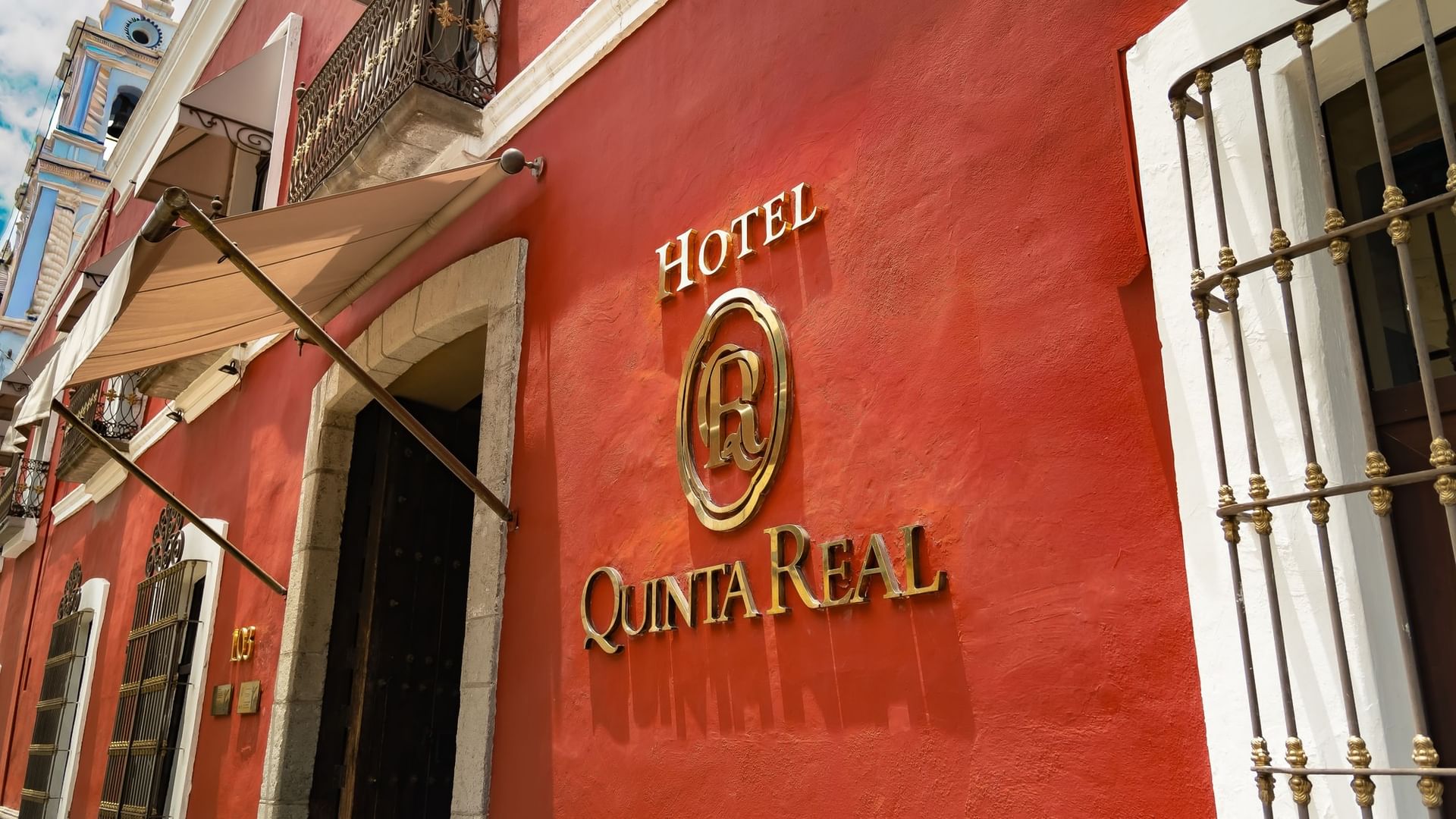 Logo dorado del hotel Quinta Real montado sobre pared texturizada roja vibrante en Quinta Real Puebla