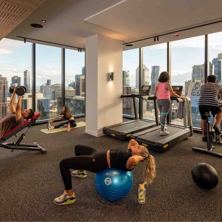 Residents exercising in a modern gym with city skyline view through large windows.