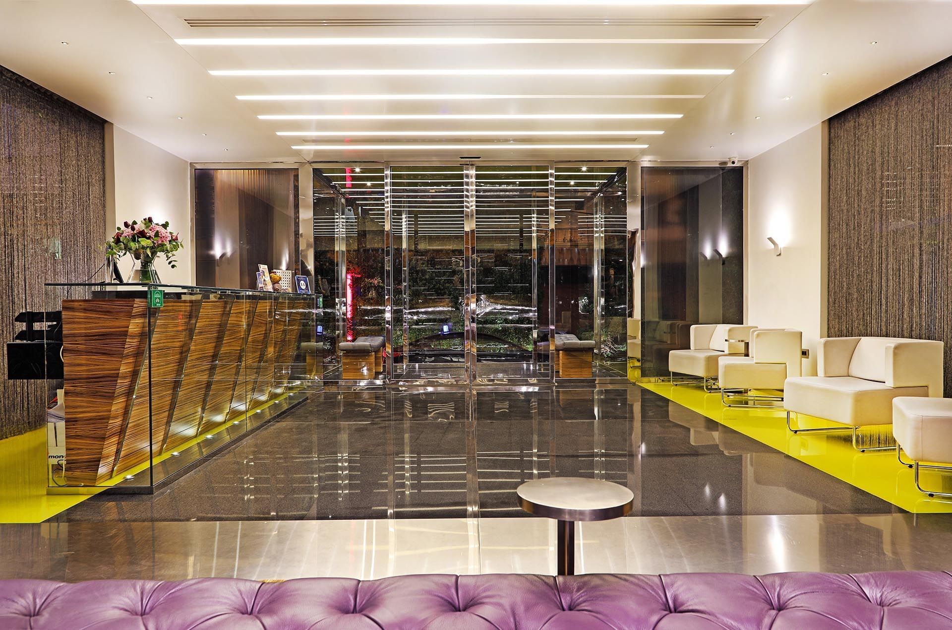 Glass entry doors by a purple leather bench under linear ceiling lights at Warwick Stone 55 - Beirut