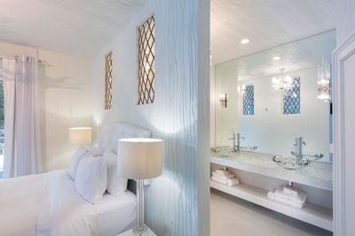 Elegant bedroom with a white bed and adjoining modern bathroom in The Mill of the Frozen Falls at The Roxbury