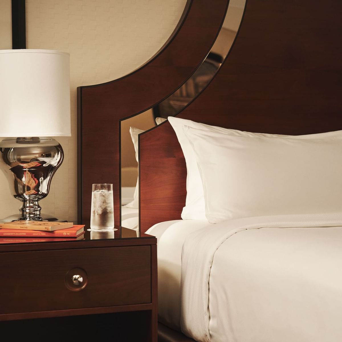 Bedroom with wooden bed, white bedding, and nightstand with lamp, glass, and book.