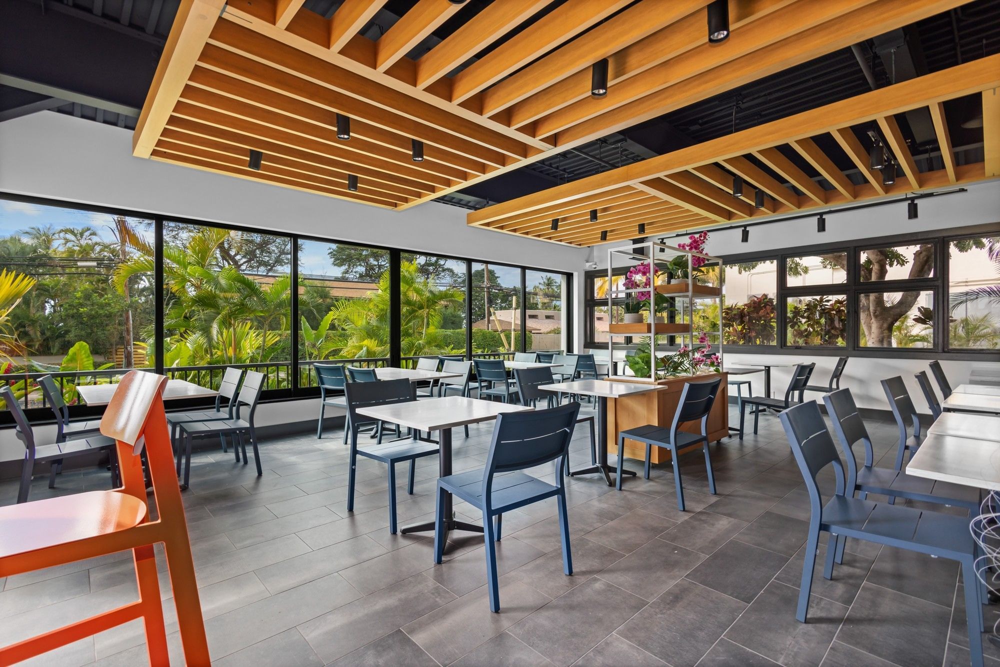 A bright and airy dining area with tables and chairs, ceiling beams, and large windows.