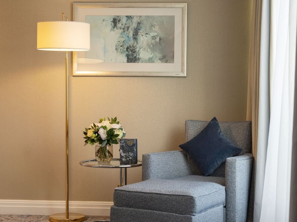 Grey armchair with a blue pillow by a glass table under a lamp in The Champs-Élysées Suite at Warwick Paris Champs Elysées
