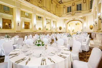 Banquet hall with white-clothed tables, floral centerpieces, and ornate gold decor at Polonia Palace Hotel