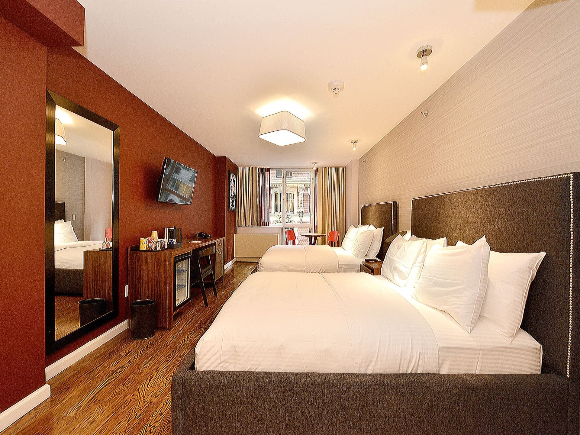 A hotel room with a double bed, desk, mini fridge, and window