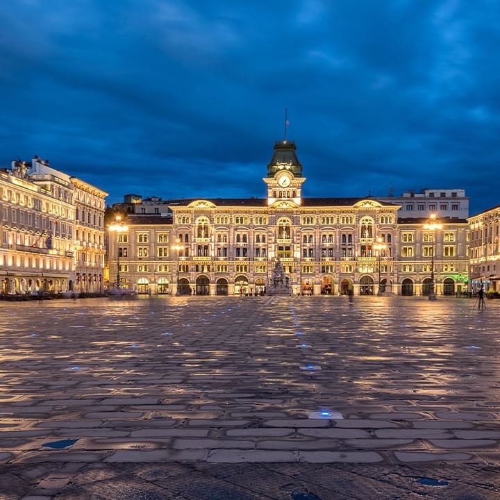 Illuminated main square with historic buildings at twilight in Trieste.