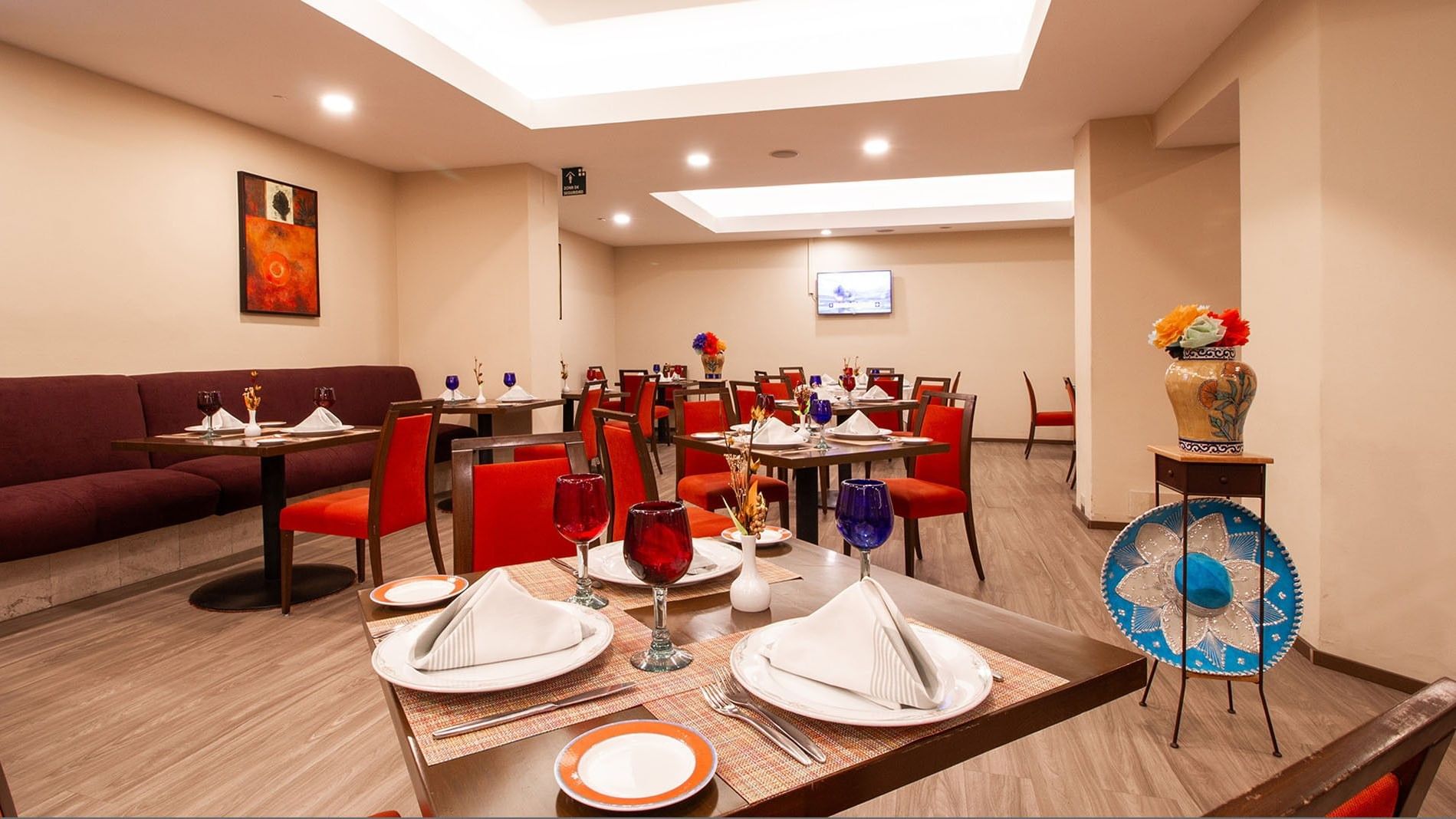 Elegant dining room with set tables and a vibrant painting at Camino Real Aeropuerto Mexico in Ciudad de Mexico.