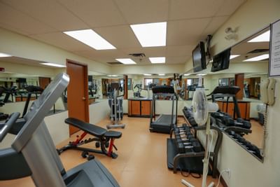 Fitness center with treadmills by a mirrored wall, black dumbbell racks under a fan at Glenmore Inn & Convention Centre
