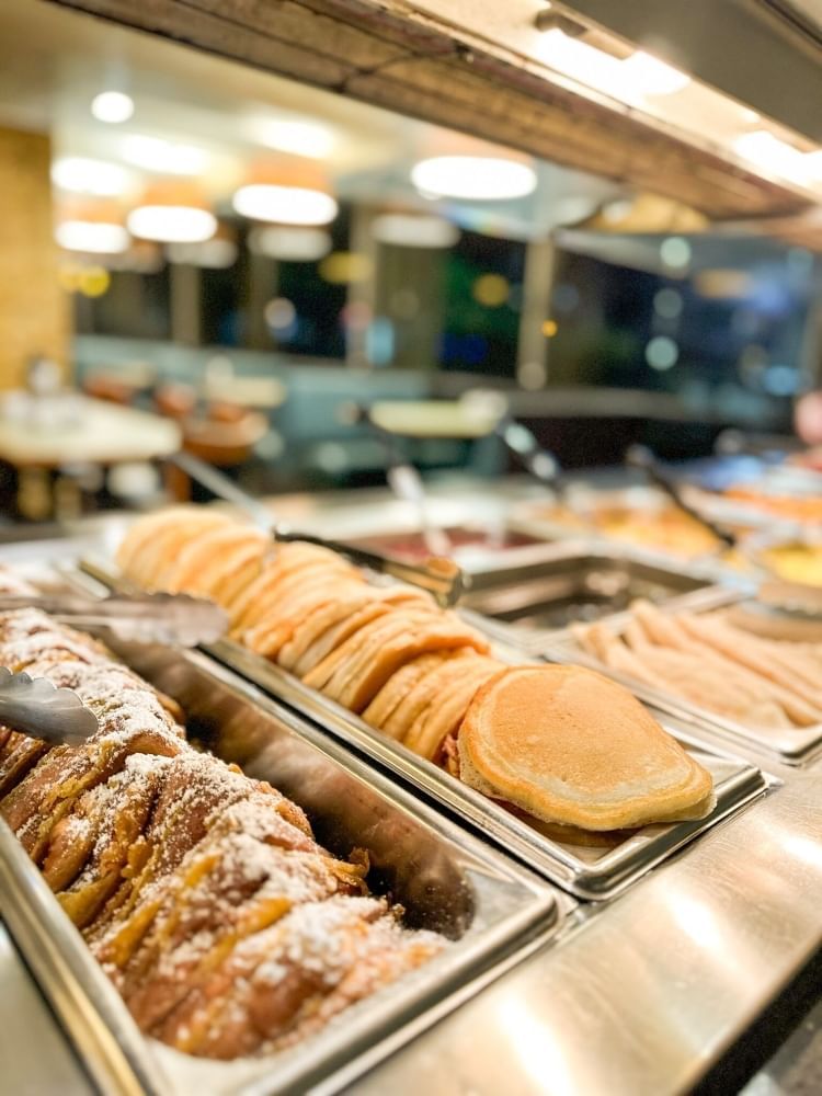 A silver buffet table with trays of French toast, pancakes, and other breakfast fare at Plaza Garden at Rosen Inn at Pointe Orlando.  