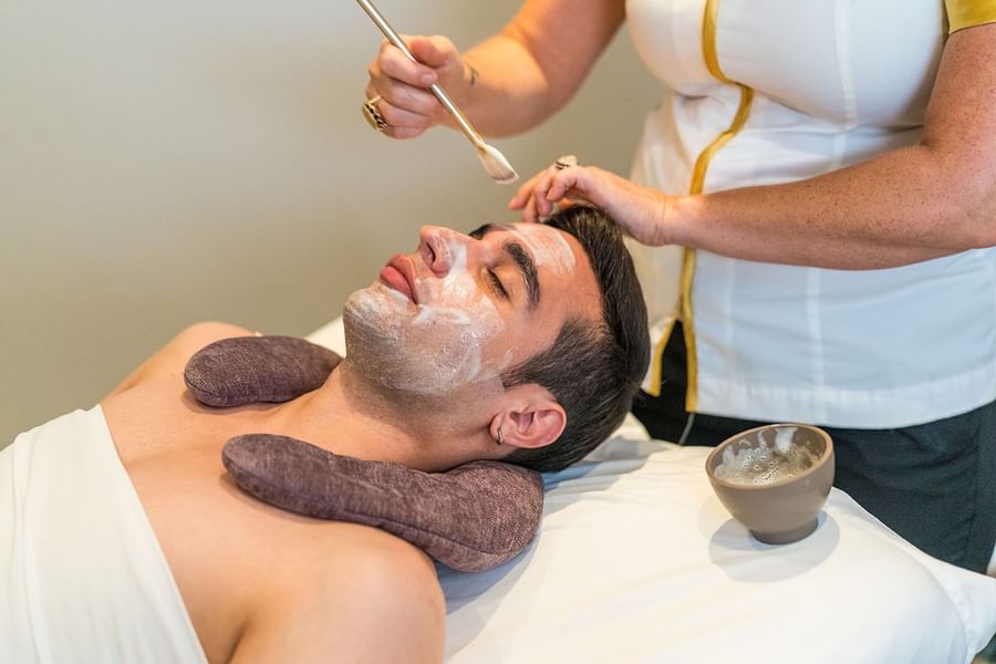 Man receiving a facial by a therapist under a soft light in a tranquil treatment room at Warwick Melrose Dallas