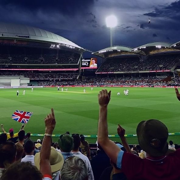 Cricket players in action during a Test Match at Adelaide Oval with a crowd watching under blue skies