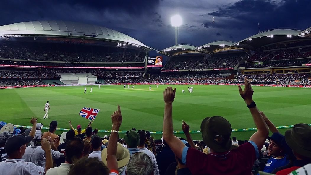 Cricket players in action during a Test Match at Adelaide Oval with a crowd watching under blue skies