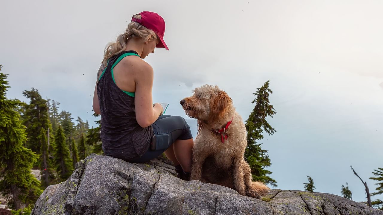 Woman resting with a Labradoodle-type dog on a rock at Skaha Bluffs Provincial Park near Coast Penticton Hotel