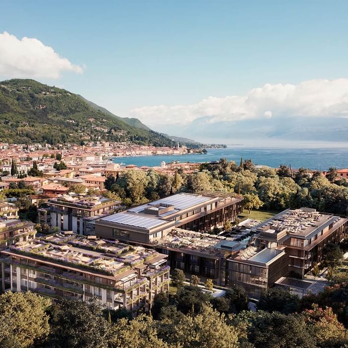Vista aerea del complesso residenziale con tetti verdi e solari, circondato da alberi e con vista sul lago.