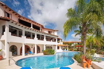 White resort building with arches beside a curved swimming pool and a tall green palm tree at Sugar Cane Club Hotel & Spa