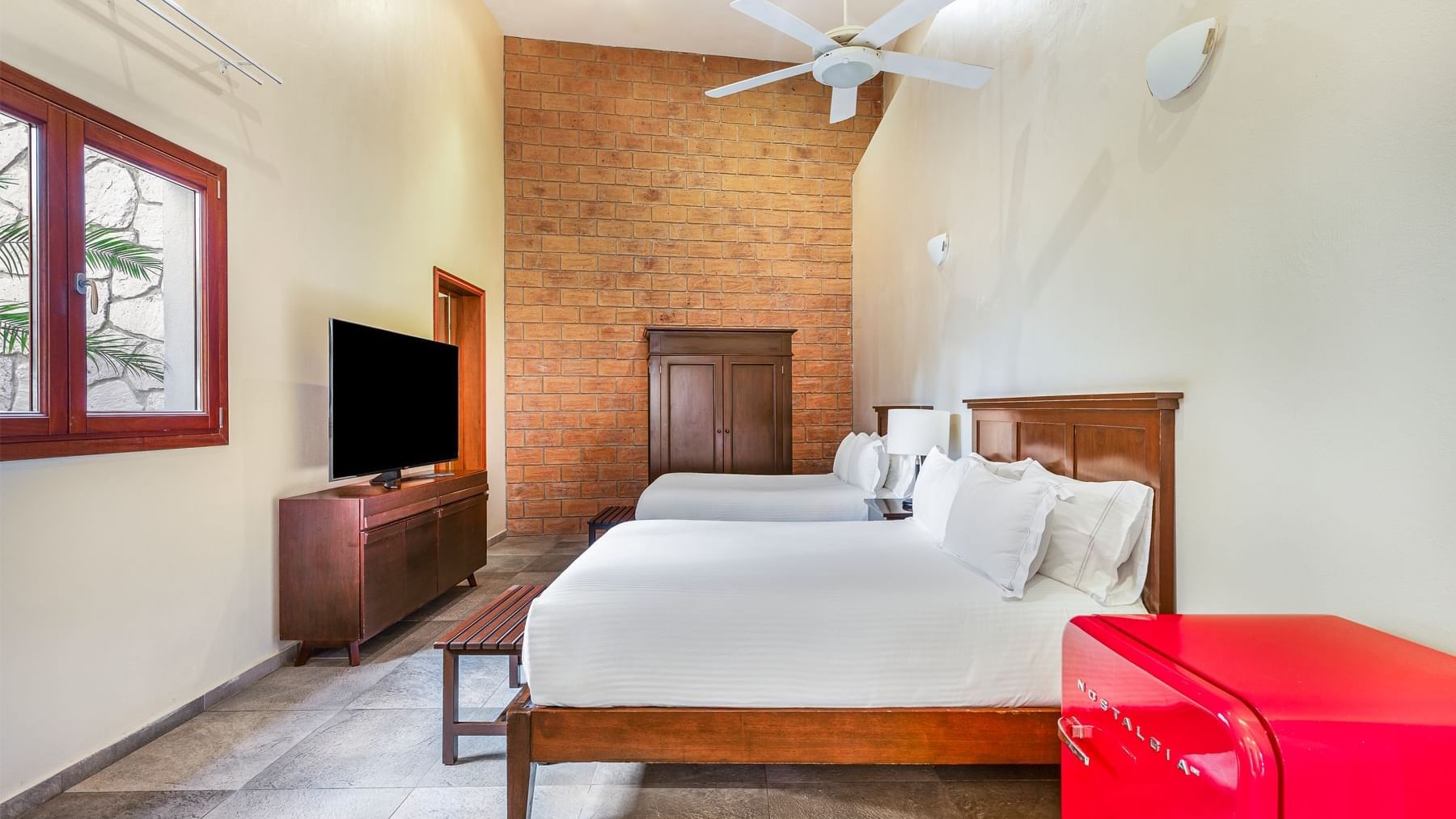 TV facing two beds and a rustic brick wall in a room at Curamoria Collection