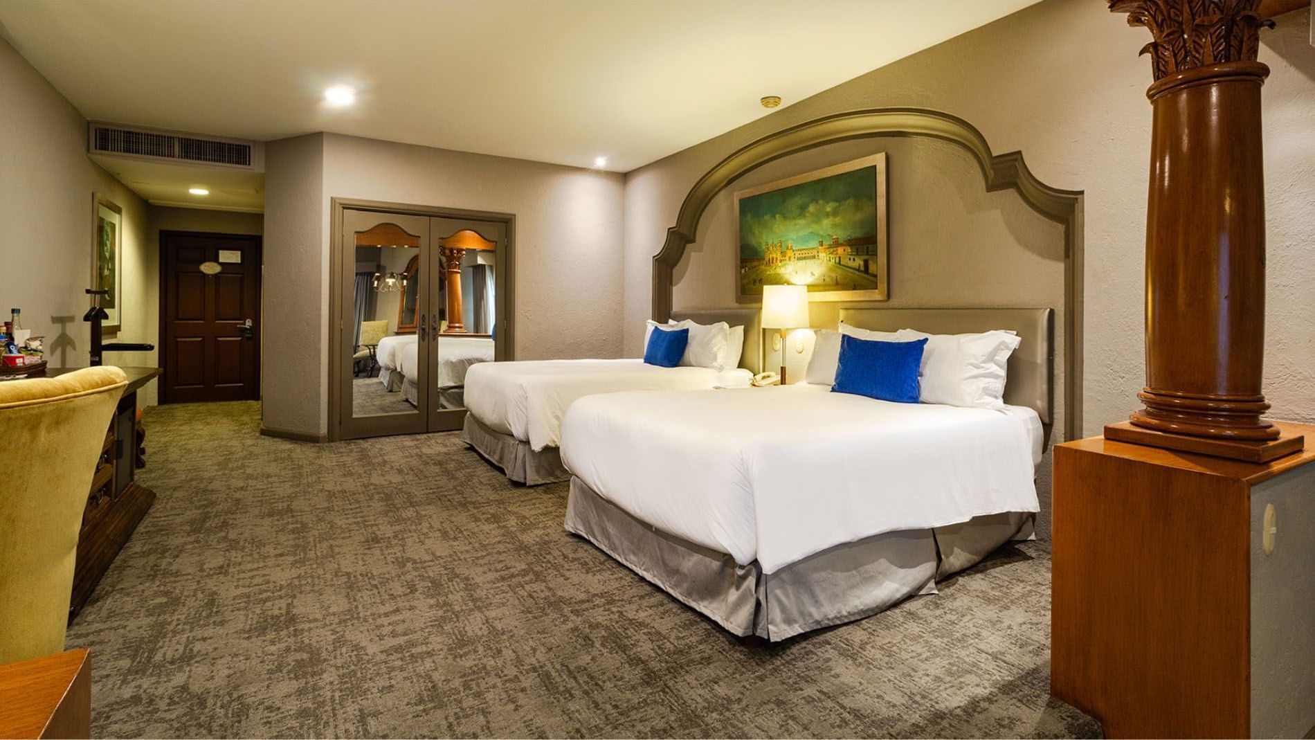 2 Double Grand Class beds with decorative wall molding and a large city plaza painting at Quinta Real Guadalajara