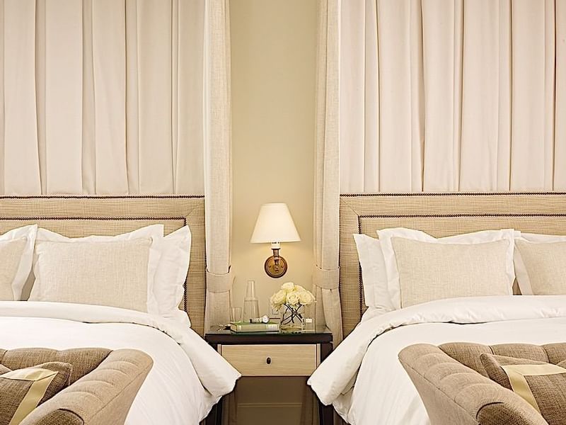 Elegant twin beds with neutral tones and bedside table at El Prado Hotel, offering serene comfort