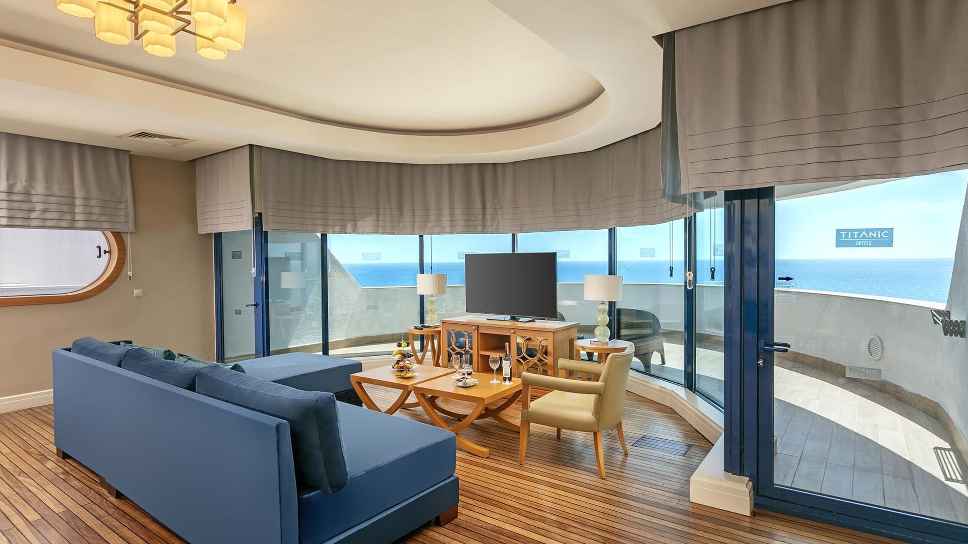 Гостиная в Titanic Deluxe Lara – Admiral Suite с видом на море, синим диваном и выходом на балкон.