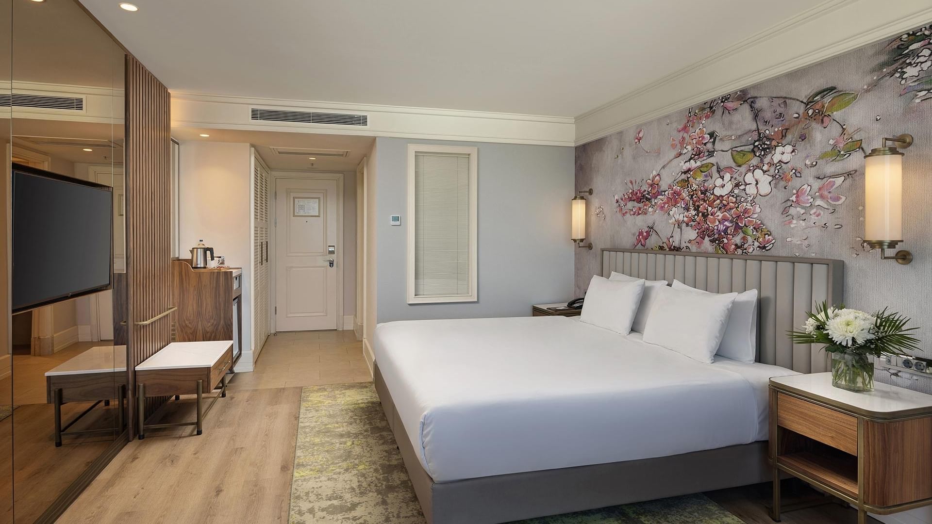 Deluxe Sea View Room with a large bed, floral wall art, wooden floors, and a vase with flowers on the nightstand.